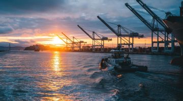 a panoramic shot of oil rigs at sea with a beautiful sunset in the background, under cloudy sky